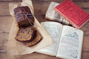 A sliced Westmorland Pepper Cake positioned next to some vintage or antique illustrated books on a wooden backdrop