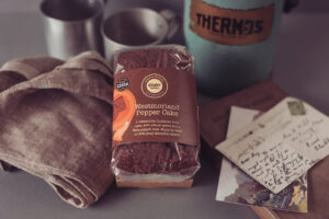 A Westmorland Pepper cake, positioned between a tea towel, a vintage thermos and some old postcards