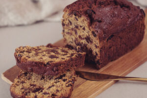 A sliced Westmorland Pepper Loaf Cake on a wooden chopping board with a rose gold butter knife